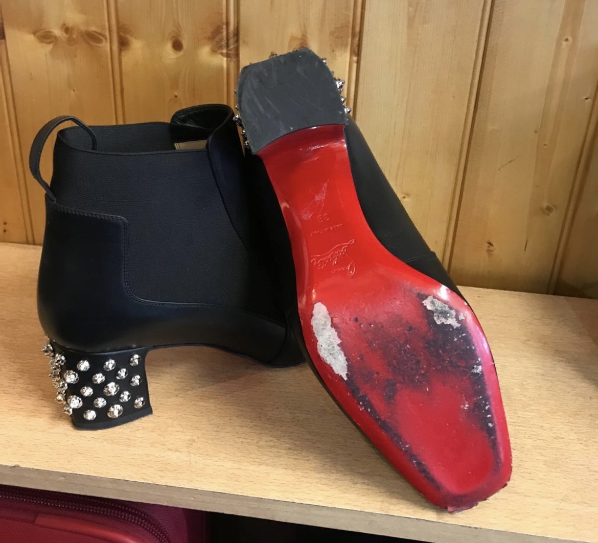 Pair of black designer ankle boots with silver-studded heels and worn red soles needing repair.