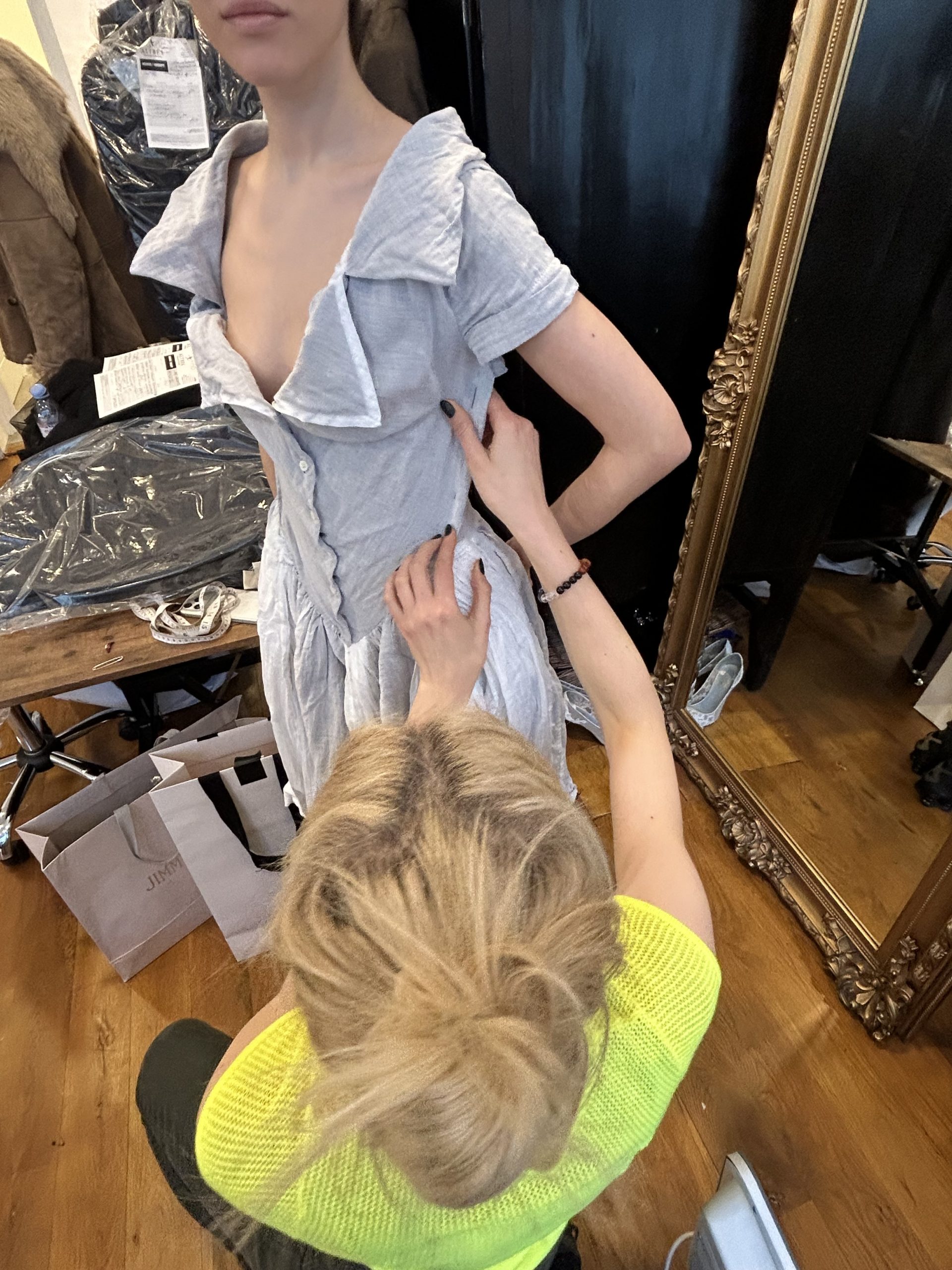 Tailor pinning a light blue linen dress on a client for bespoke luxury alterations in an atelier.