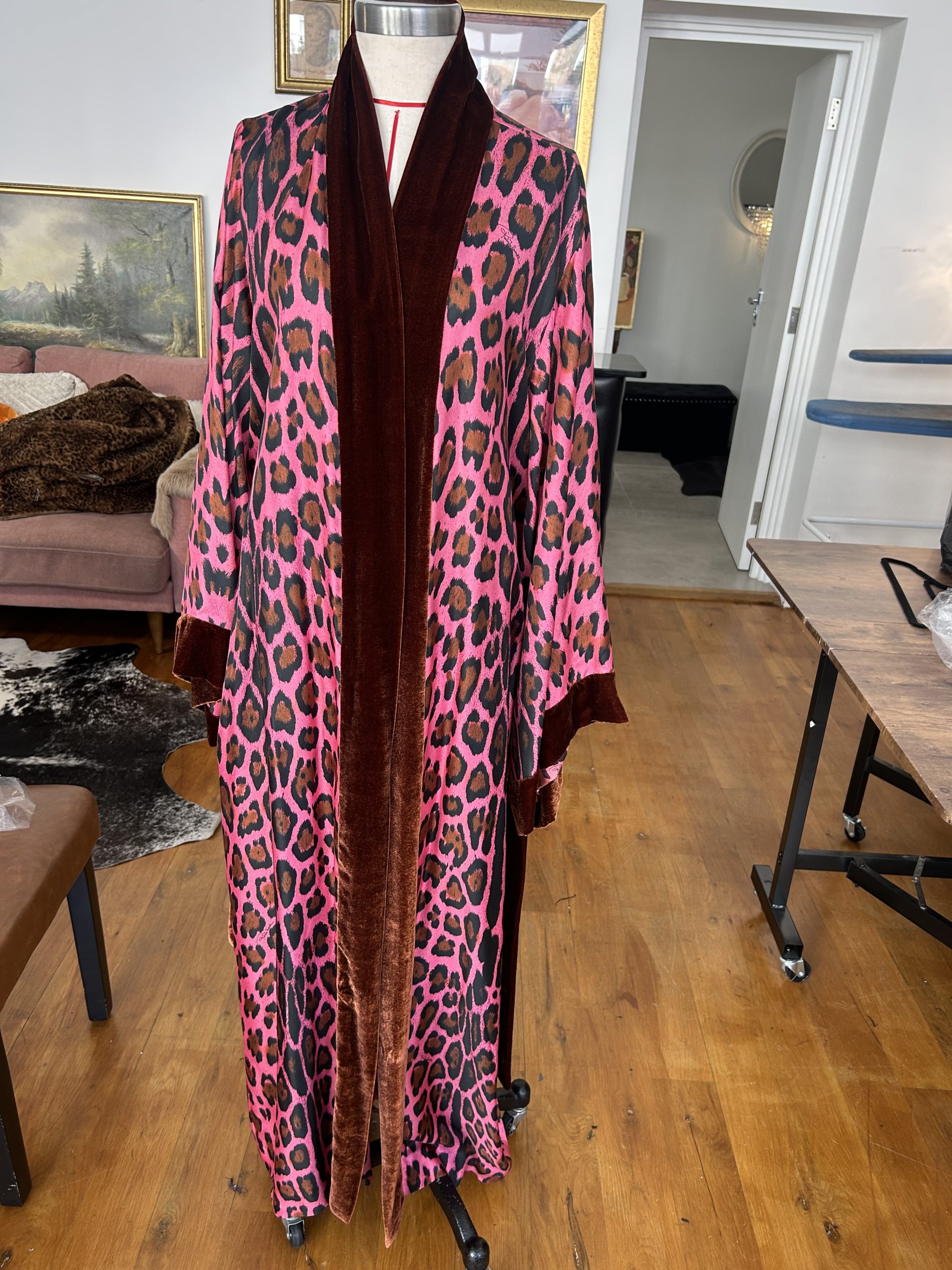 Bespoke pink leopard-print robe with dark velvet lapels displayed on a mannequin in an atelier.