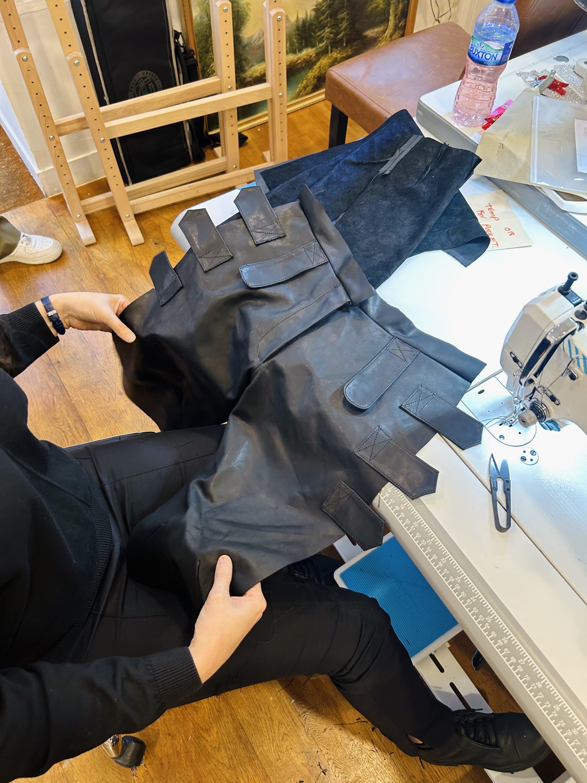 Tailor at a sewing machine holding a black leather garment piece in progress