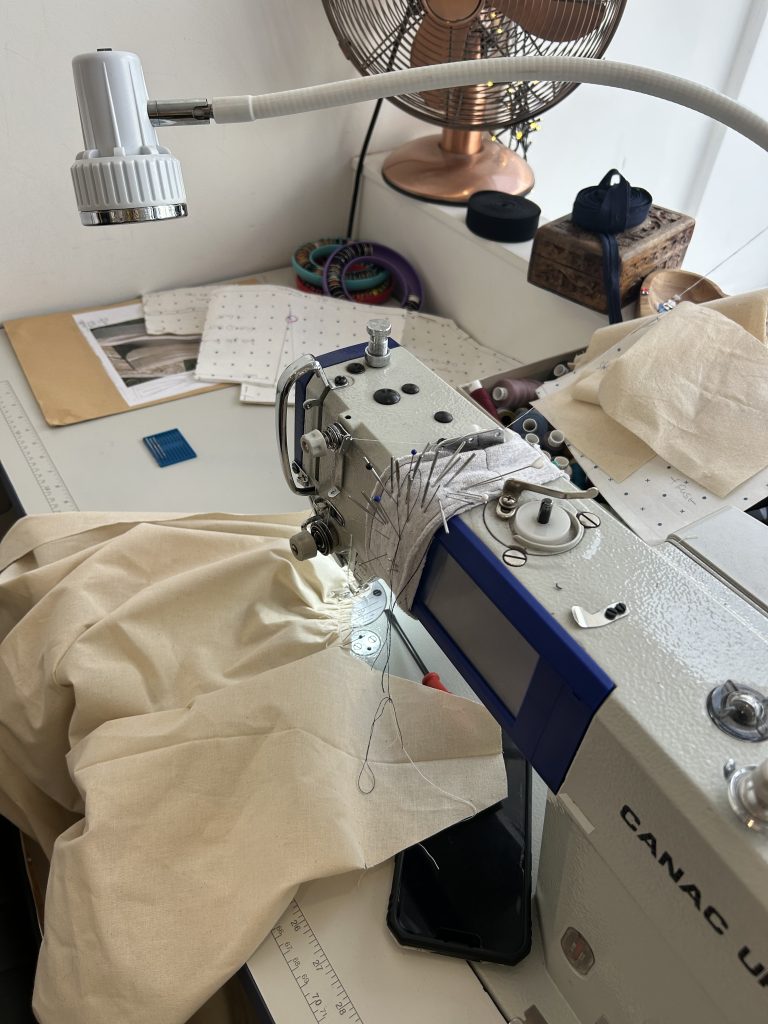 Industrial sewing machine on a workbench with cream fabric, pins and dressmaking tools