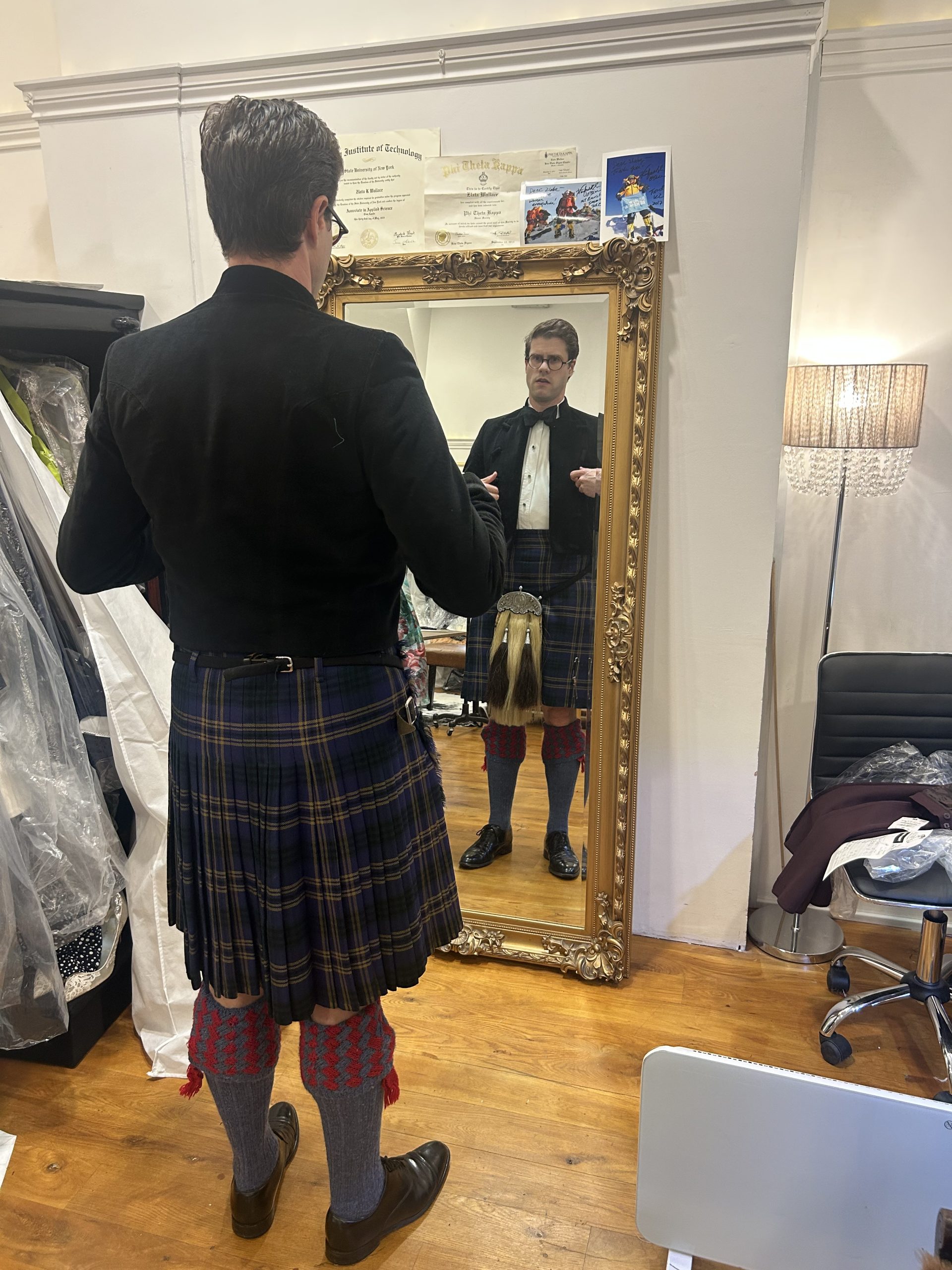 Man in Highland dress with tartan kilt and sporran checking the fit in an ornate mirror