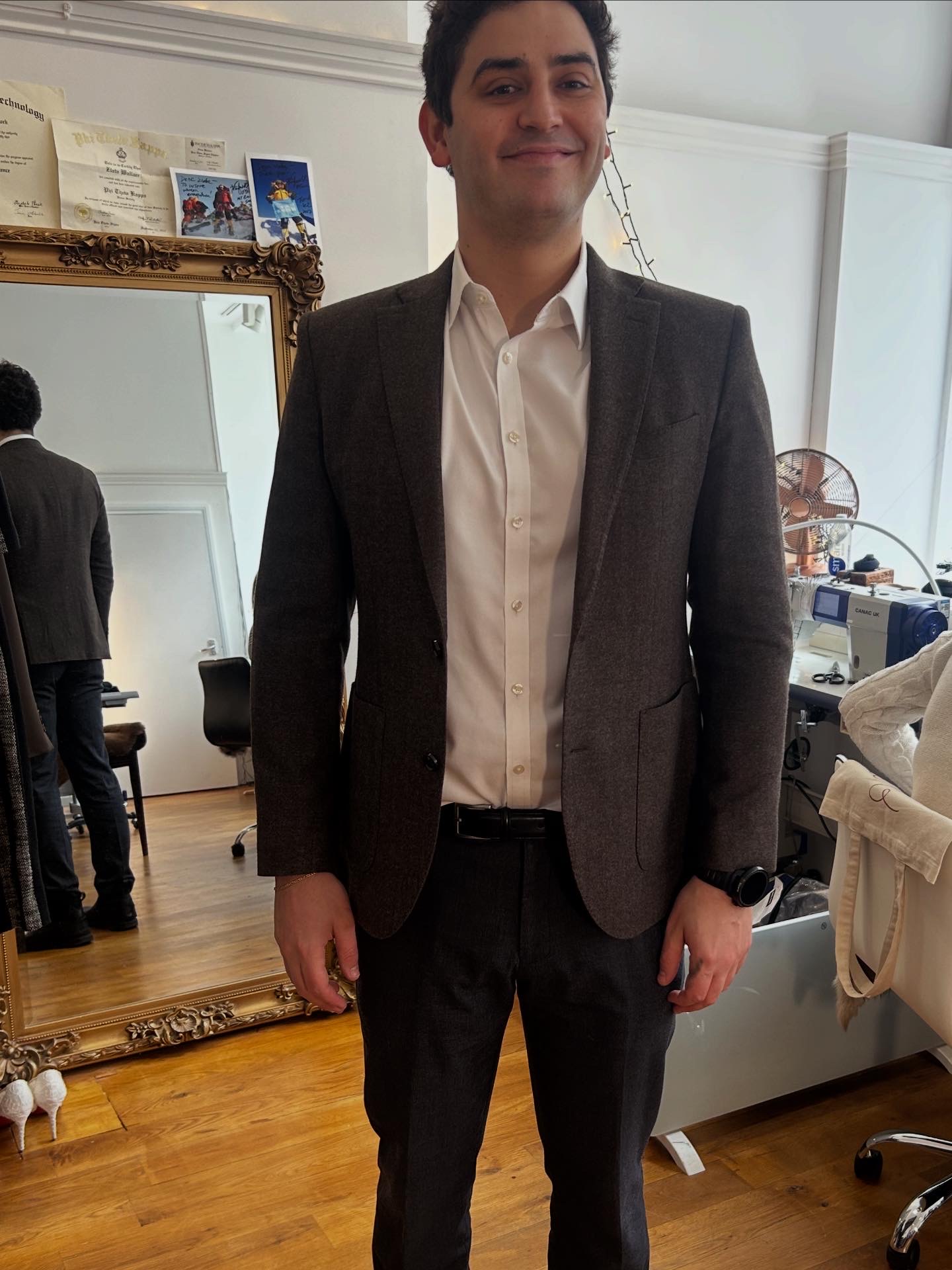 Client smiling in a dark brown textured wool jacket during a fitting at a bespoke tailoring atelier