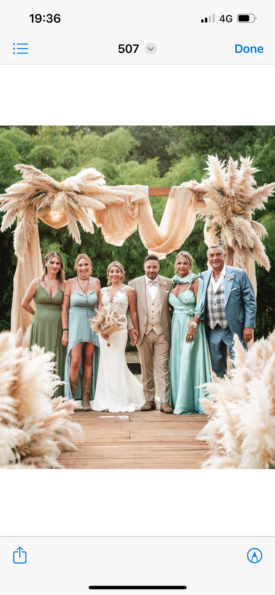 Bride in a lace mermaid wedding dress under a pampas grass arch with wedding party