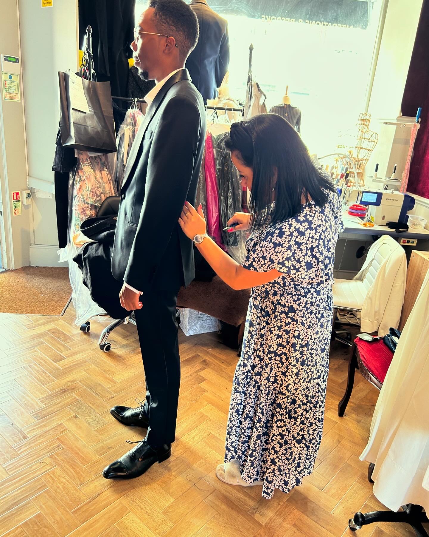 Tailor adjusting a client's black bespoke suit during a fitting session in a professional atelier