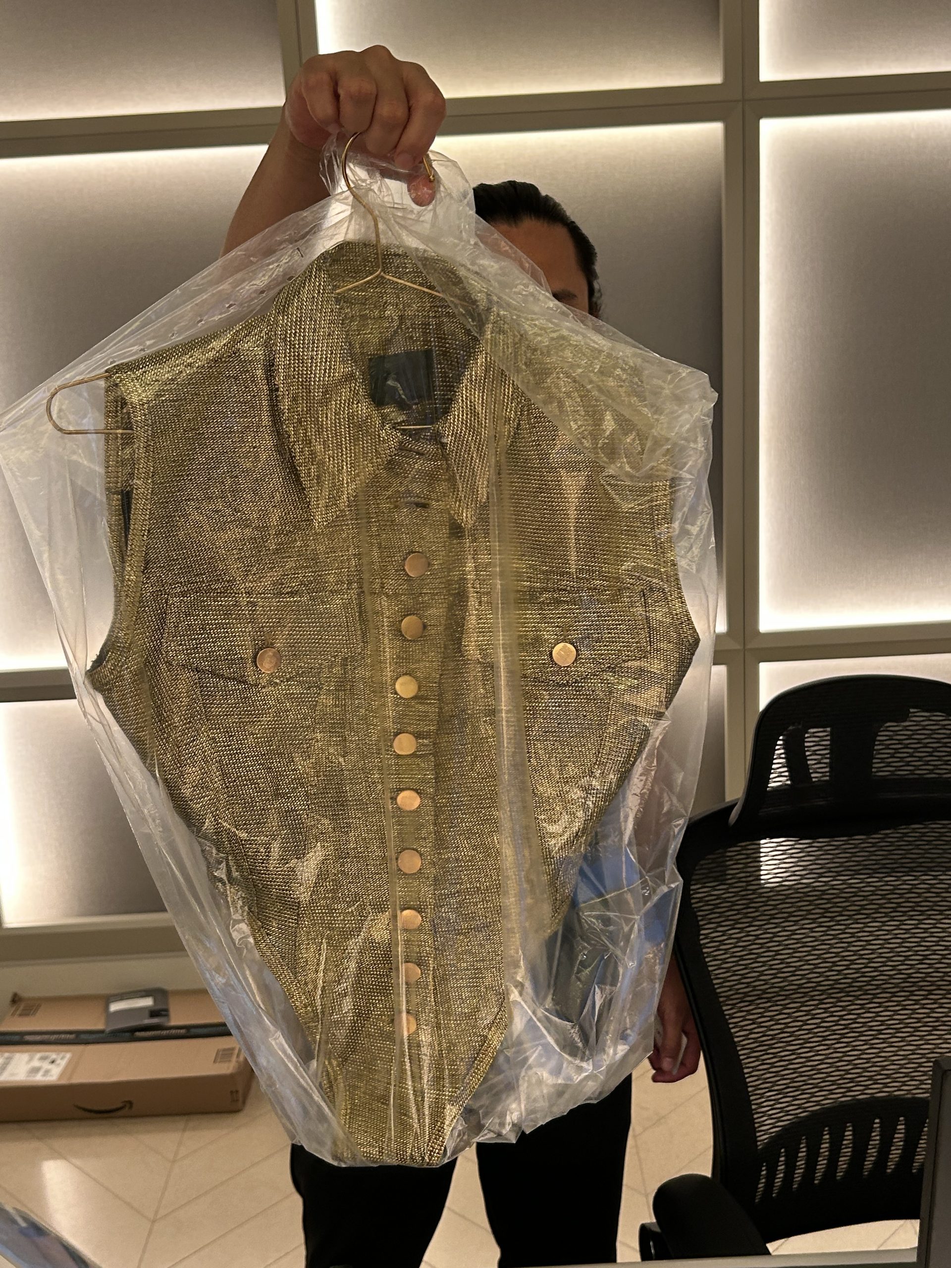 Gold metallic sleeveless bodysuit on a hanger in a protective cover for a residence fitting.