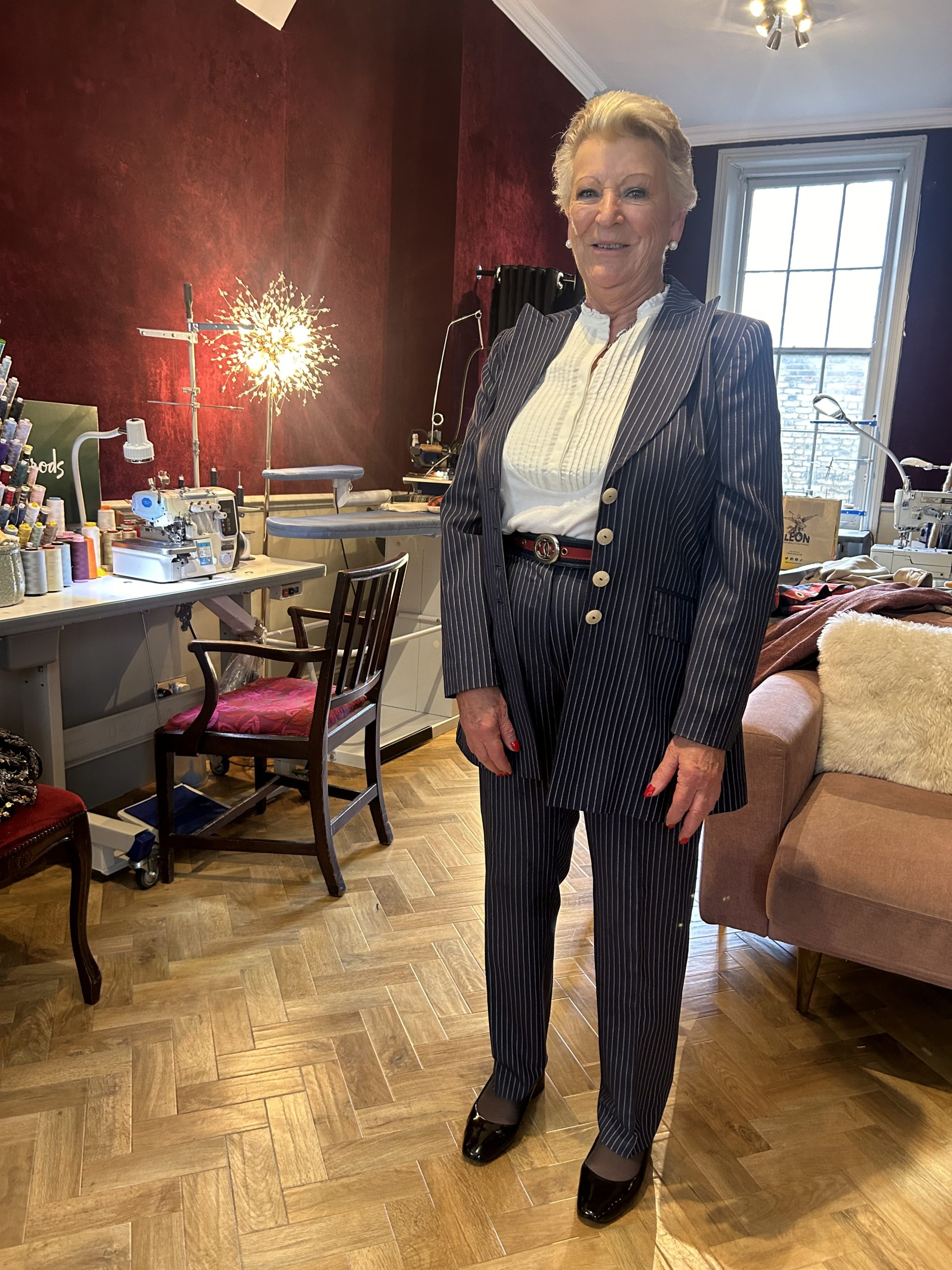 Woman posing in a navy pinstripe bespoke trouser suit with peaked lapels in a tailoring atelier