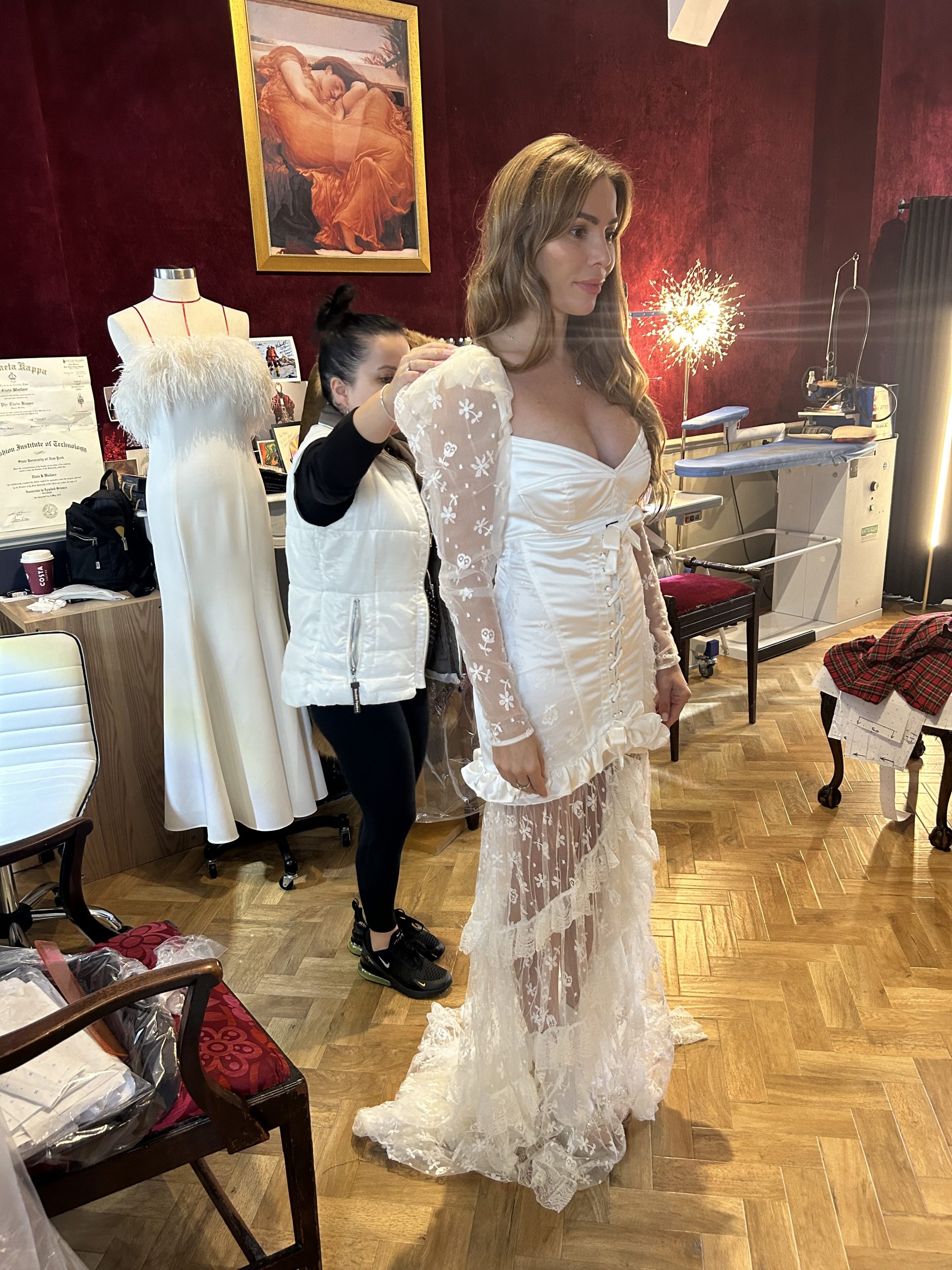 Tailor adjusting a bespoke white lace special occasion gown during a luxury atelier fitting.