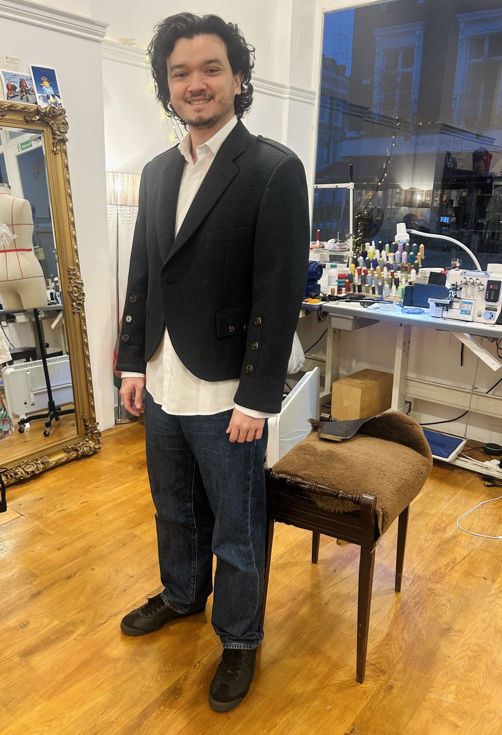 Young man in a charcoal structured bespoke jacket with epaulettes standing in a tailoring atelier