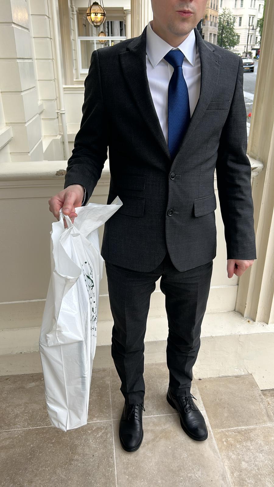 Man in a fitted charcoal suit and royal blue tie standing on townhouse steps after a residence fitting.