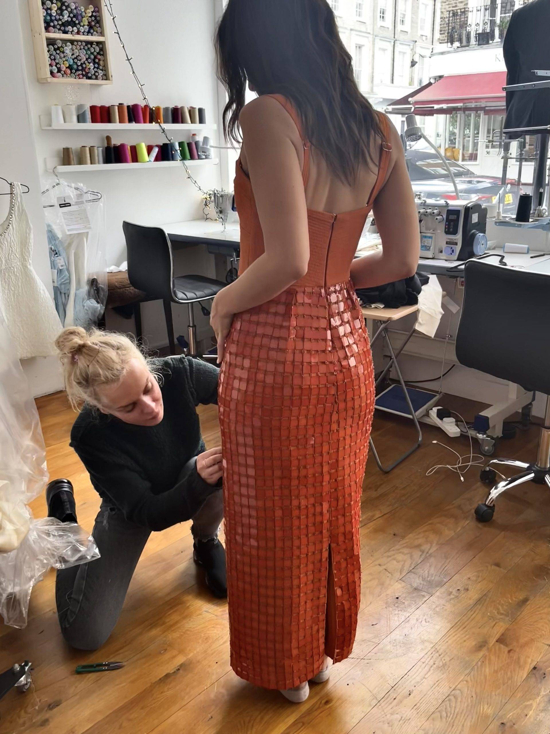 Altbes tailor kneeling to fit a bespoke orange sequin evening dress in the Pimlico atelier